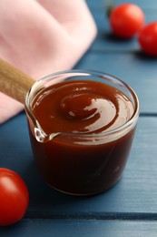 Photo of Tasty barbeque sauce and tomato on blue wooden table, closeup