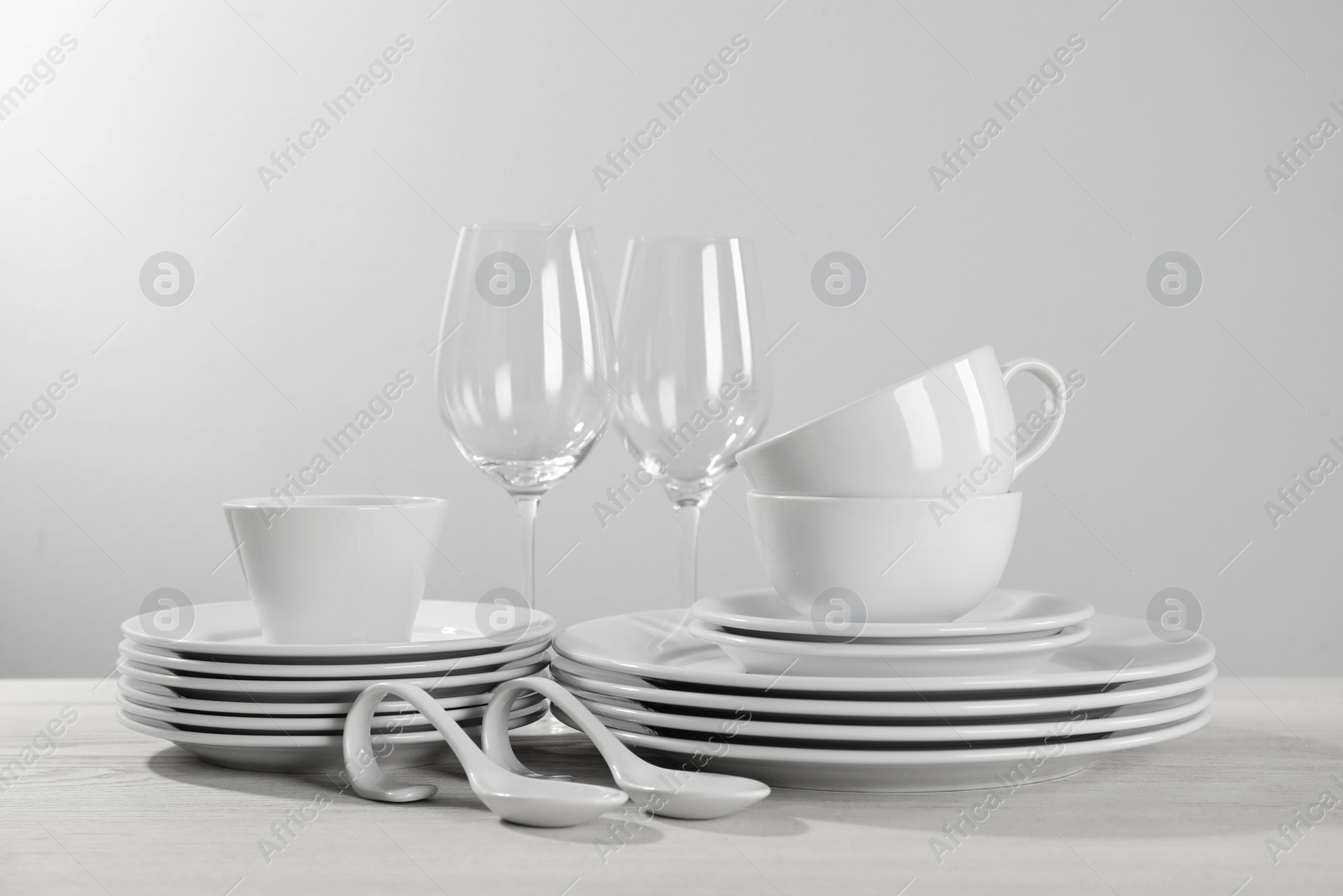 Photo of Set of clean dishware and glasses on white wooden table against light background