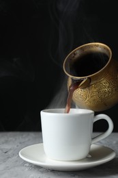 Photo of Turkish coffee. Pouring brewed beverage from cezve into cup at grey table, closeup