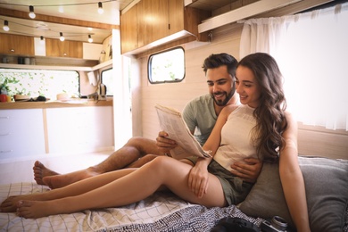 Photo of Happy young couple reading newspaper on bed in trailer. Camping vacation