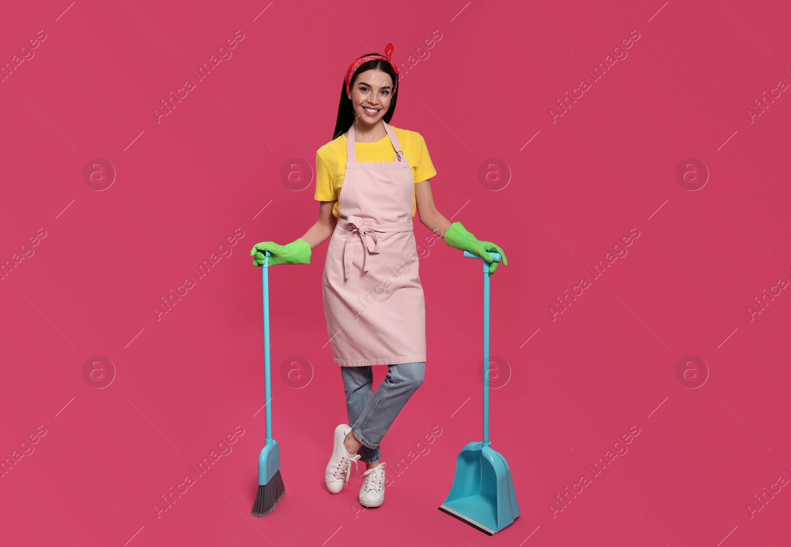 Photo of Young housewife with broom and scoop on pink background