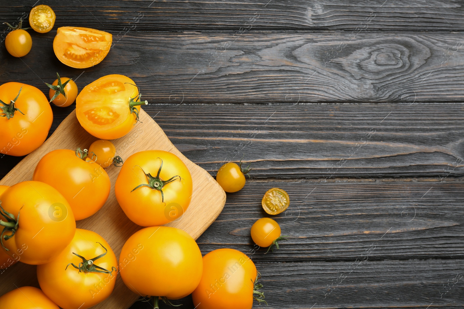 Photo of Ripe yellow tomatoes on dark wooden table, flat lay. Space for text