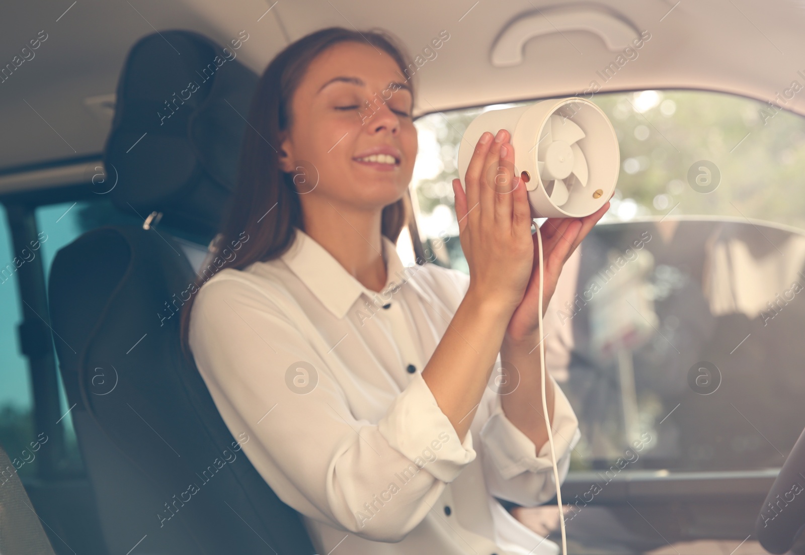 Photo of Young woman enjoying air flow from portable fan in car on hot summer day