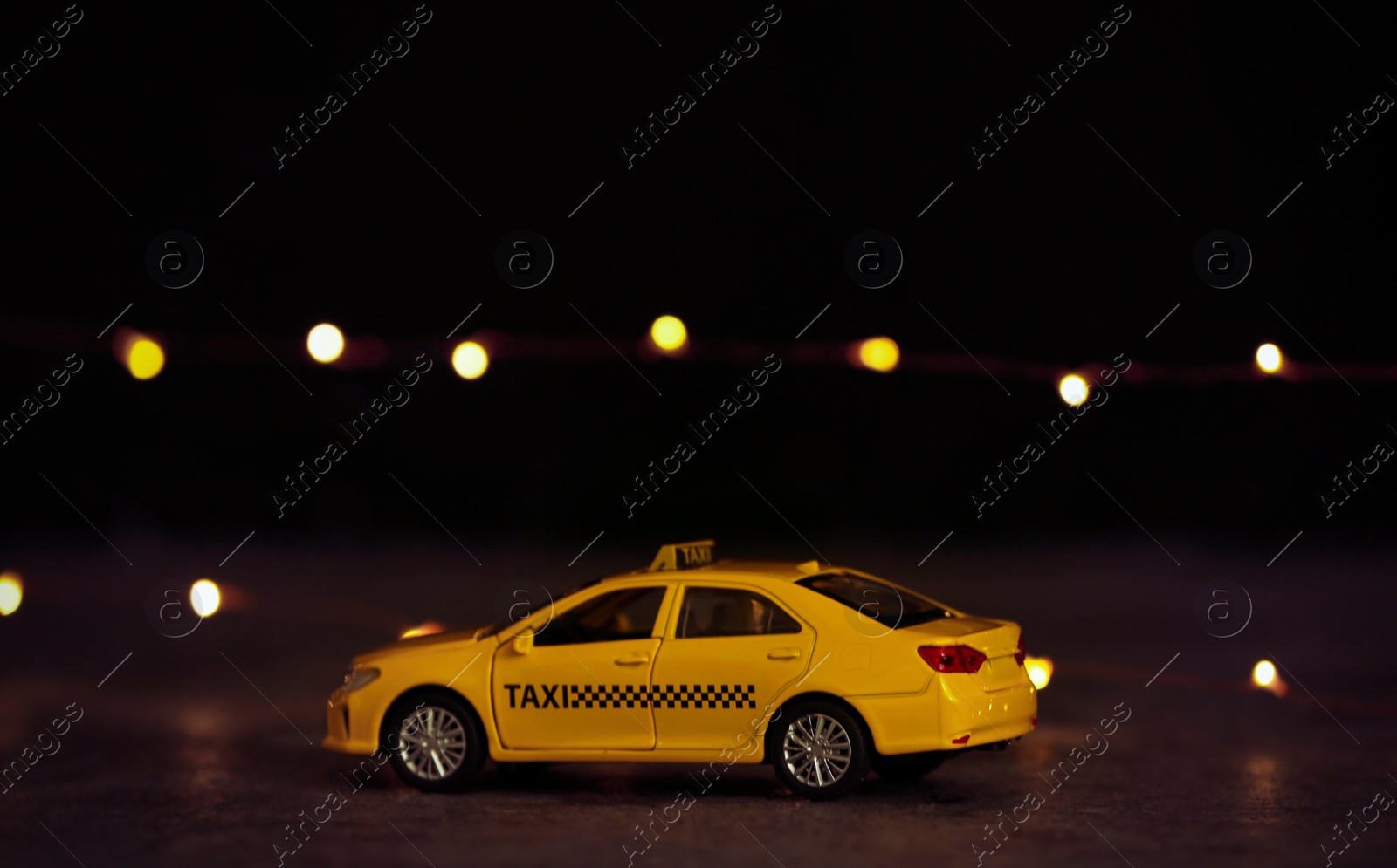 Photo of Yellow taxi car model on table against festive lights. Bokeh effect