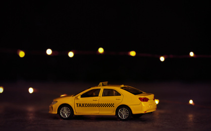 Photo of Yellow taxi car model on table against festive lights. Bokeh effect