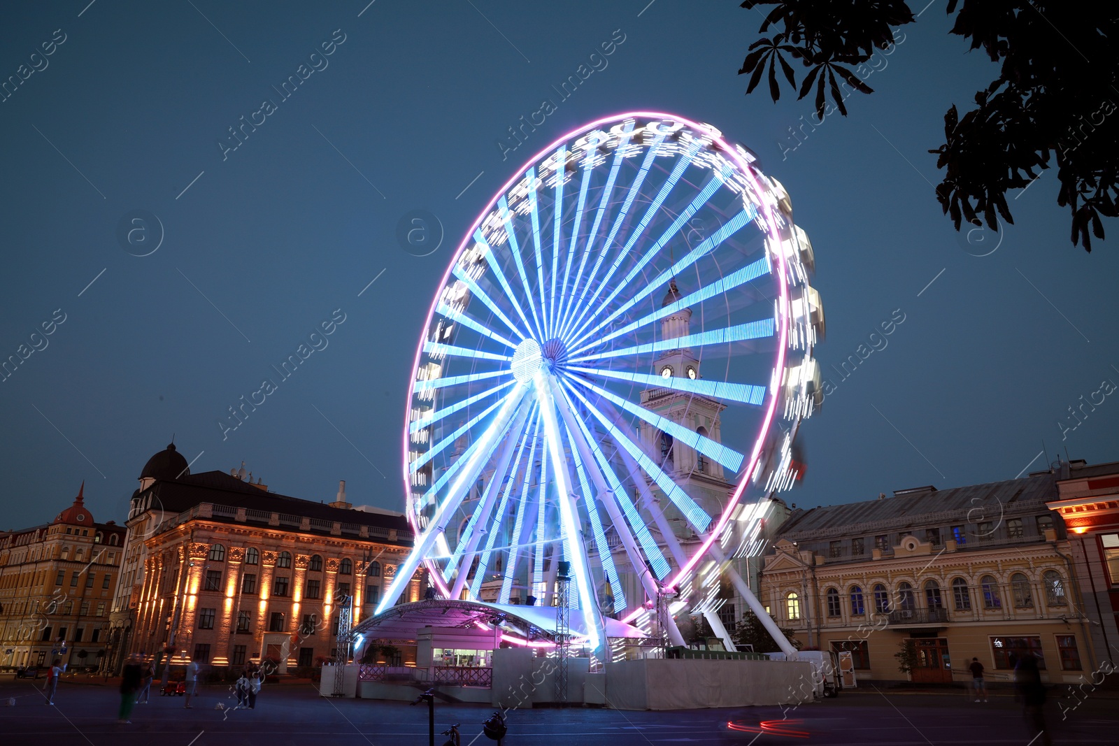 Photo of Big glowing Ferris wheel on city street at night, low angle view