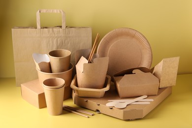 Photo of Eco friendly food packaging. Paper containers, tableware and bag on pale yellow background