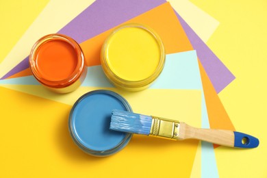 Photo of Jars of different paints and brush on color background, flat lay