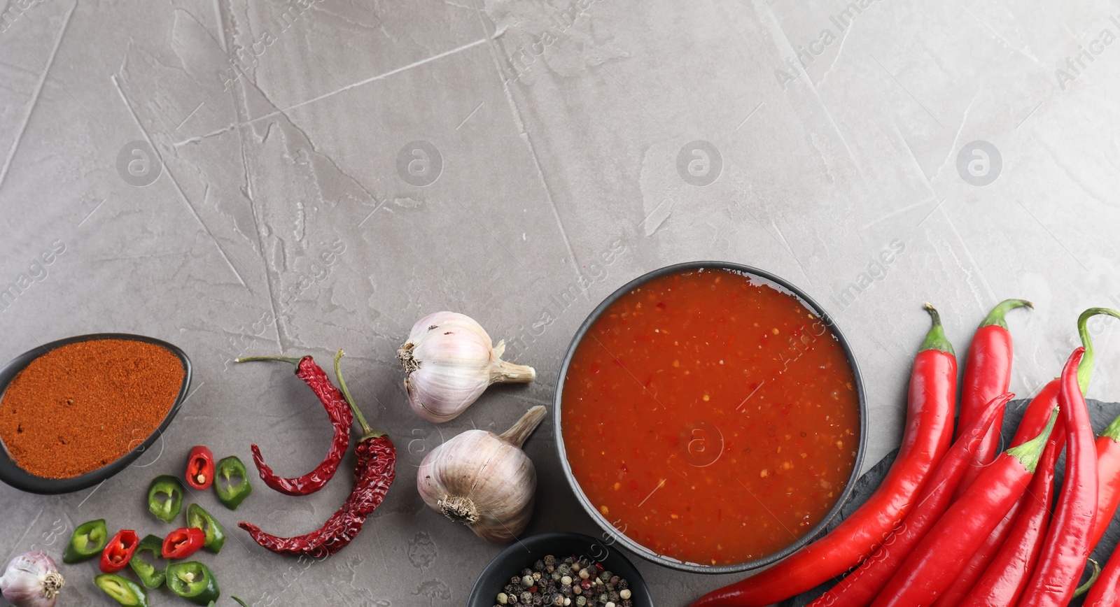 Photo of Spicy chili sauce in bowl and ingredients on grey table, flat lay. Space for text