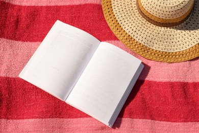 Photo of Open book and hat on striped beach towel, top view