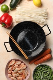 Black wok, chopsticks and products on color table, flat lay