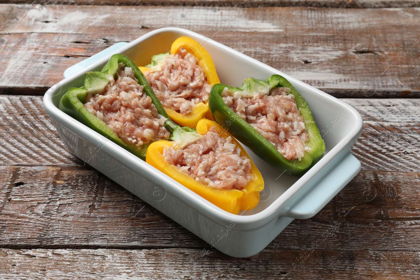 Photo of Raw stuffed peppers in dish on wooden table