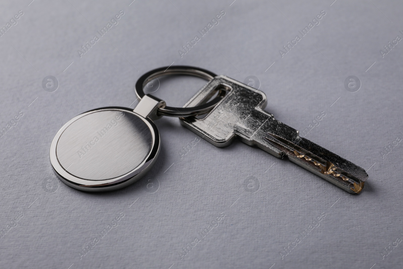 Photo of Key with metallic keychain on light grey background, closeup