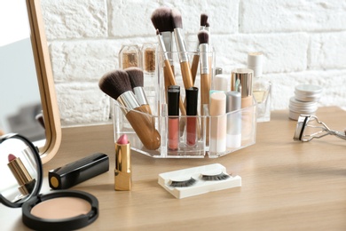 Organizer with cosmetic products for makeup on table near brick wall