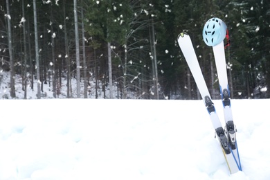 Pair of skis with helmet in snow near forest, space for text. Winter vacation