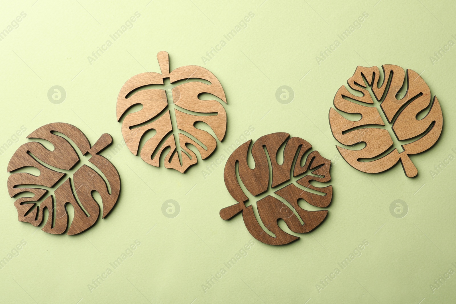 Photo of Leaf shaped wooden cup coasters on pale green background, flat lay