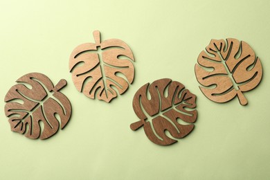 Leaf shaped wooden cup coasters on pale green background, flat lay