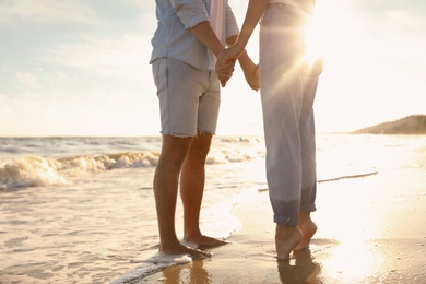 Photo of Couple on sandy beach near sea at sunset, closeup of legs