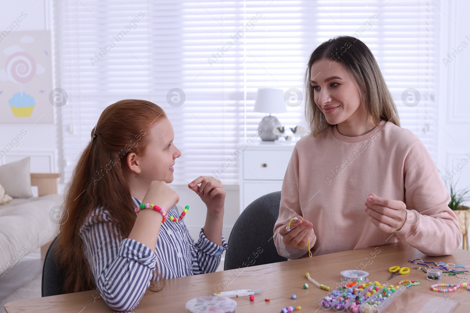 Photo of Happy mother with her daughter making beaded jewelry at home