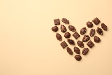 Heart made with delicious chocolate candies on beige background, top view. Space for text