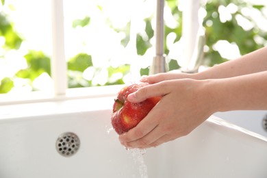 Photo of Woman washing fresh red apple in kitchen sink, closeup. Space for text