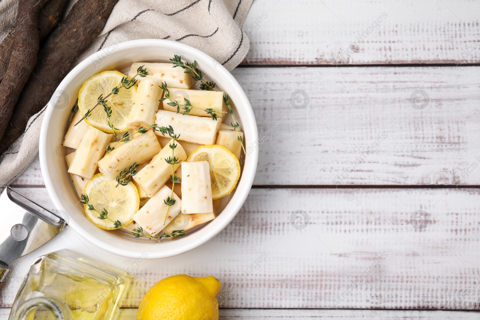 Photo of Dish with raw salsify roots, lemon and thyme on white wooden table, flat lay. Space for text