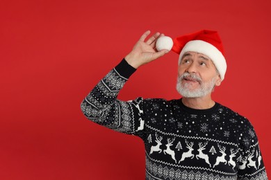 Photo of Senior man in Christmas sweater and Santa hat on red background. Space for text