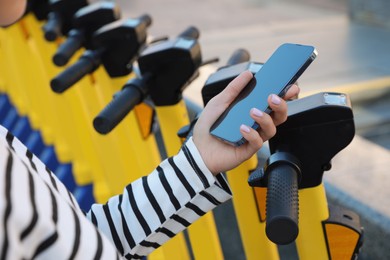 Photo of Woman using smartphone to pay and unblock electric kick scooter outdoors, closeup