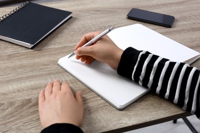 Woman writing in notebook at wooden table, closeup