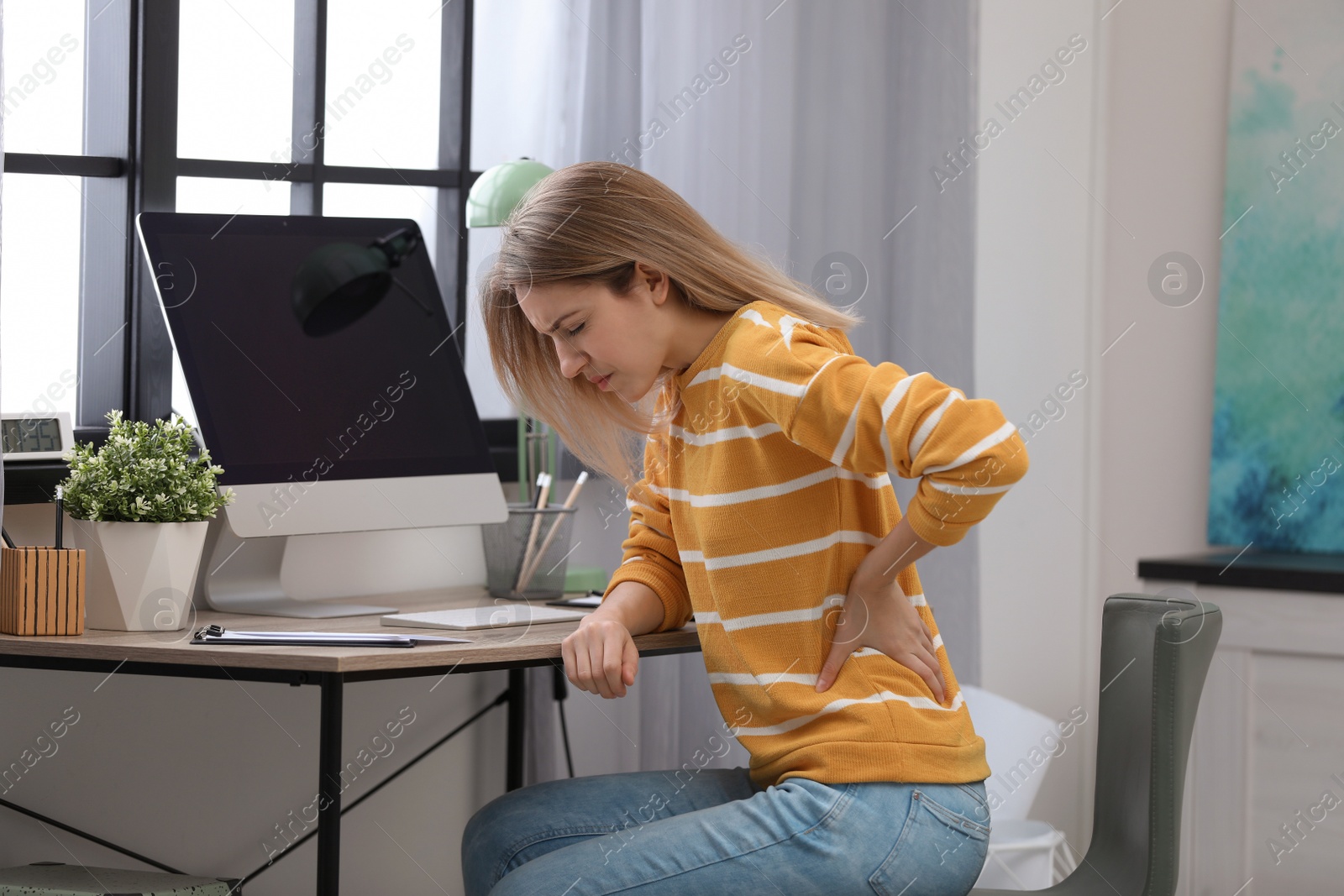 Photo of Young woman suffering from back pain in office