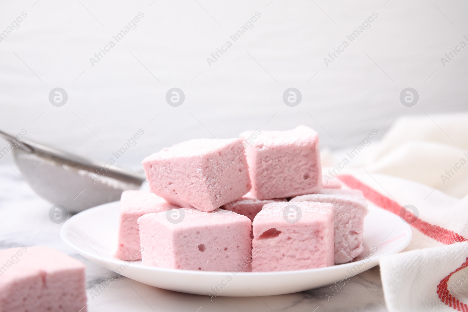 Photo of Plate of delicious sweet marshmallows with powdered sugar on white marble table, closeup