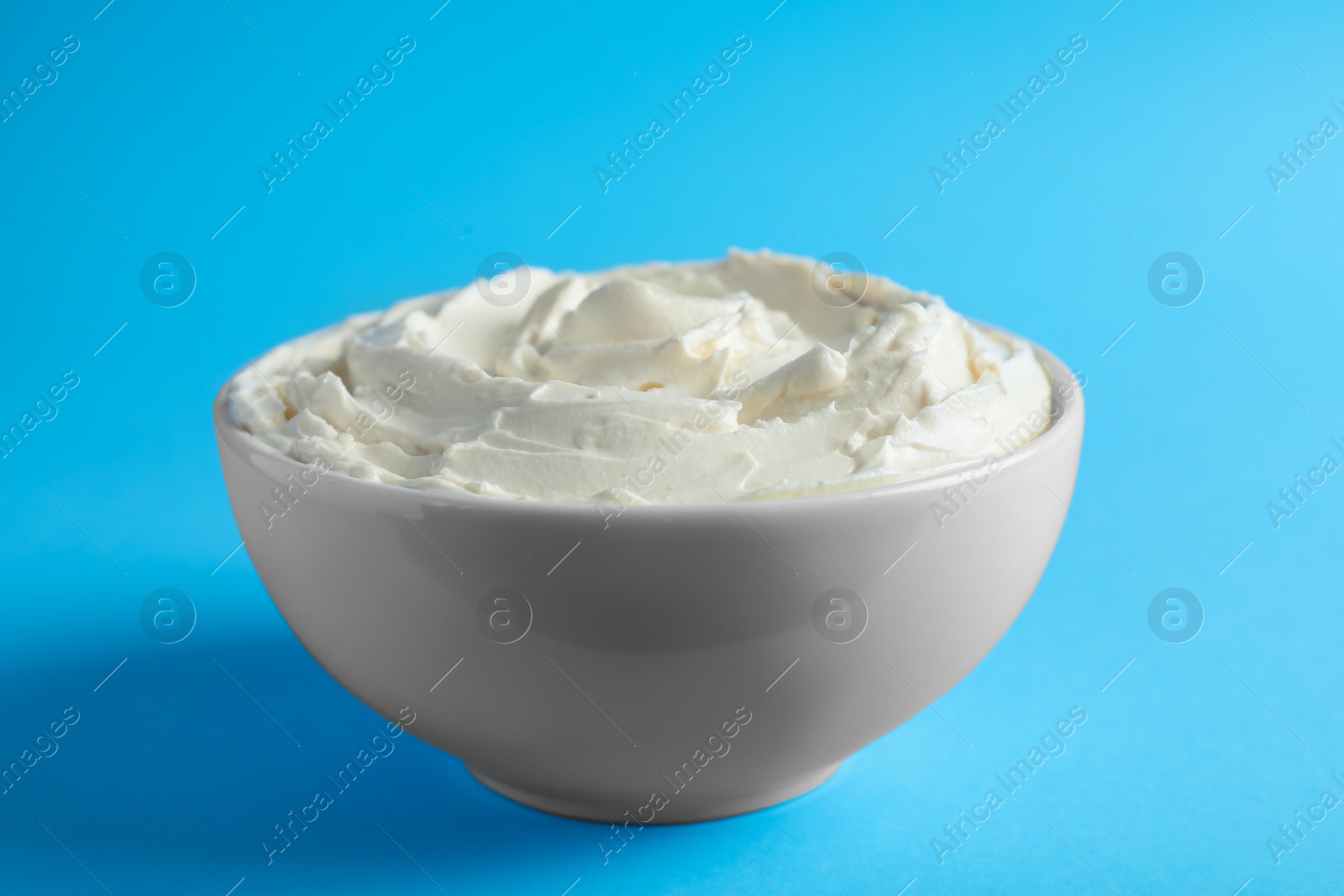 Photo of Bowl of tasty cream cheese on light blue background