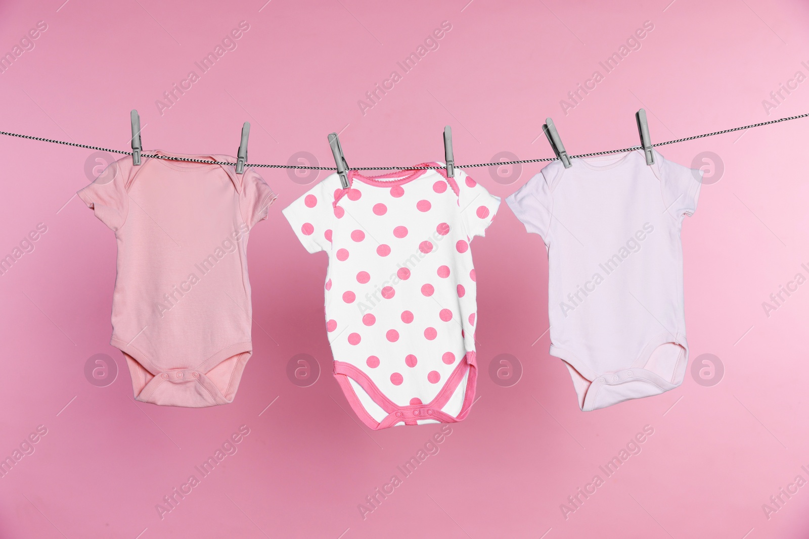 Photo of Baby onesies drying on laundry line against pink background