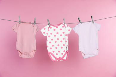 Photo of Baby onesies drying on laundry line against pink background