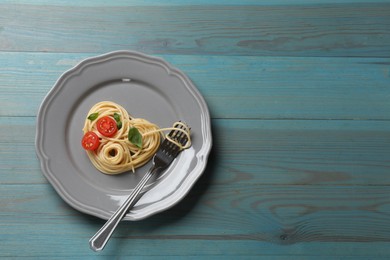 Photo of Heart made of tasty spaghetti, fork, tomato and basil on light blue wooden table, top view. Space for text
