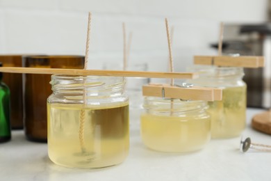 Photo of Glass jars with melted wax on white table. Handmade candles