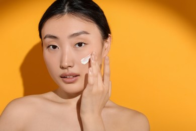 Photo of Beautiful young woman in sunlight with sun protection cream on her face against orange background, space for text
