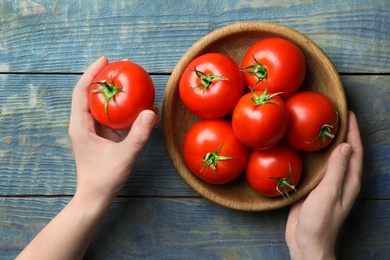 Photo of Woman with ripe tomatoes at blue wooden table, top view