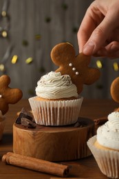 Woman decorated tasty Christmas cupcake with gingerbread man cookie at wooden table, closeup
