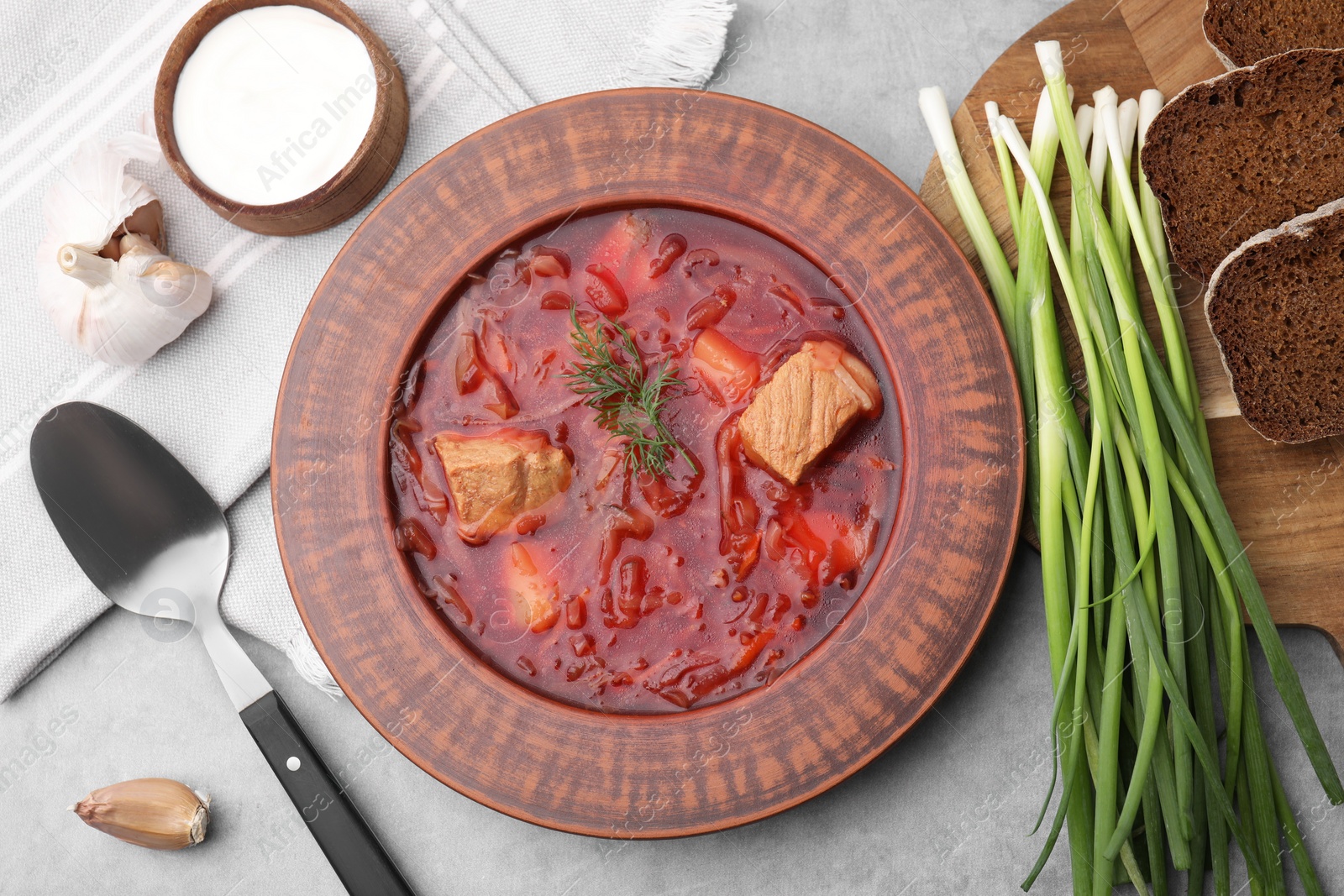 Photo of Bowl of delicious borscht, garlic, sour cream and onions on light grey table, flat lay