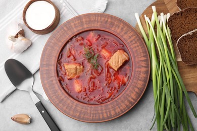 Photo of Bowl of delicious borscht, garlic, sour cream and onions on light grey table, flat lay
