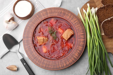 Bowl of delicious borscht, garlic, sour cream and onions on light grey table, flat lay