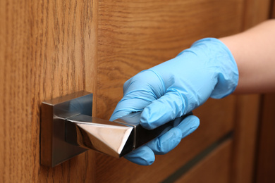 Photo of Woman in protective gloves opening wooden door, closeup