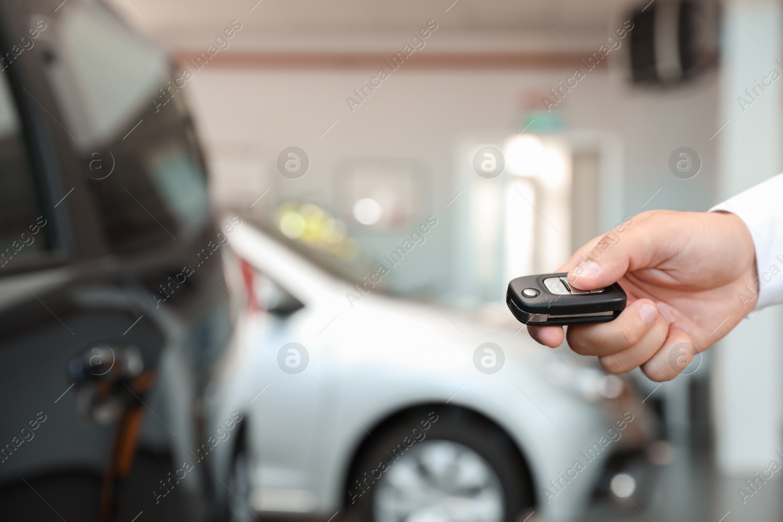 Photo of Young man turning off alarm system with car key indoors, closeup