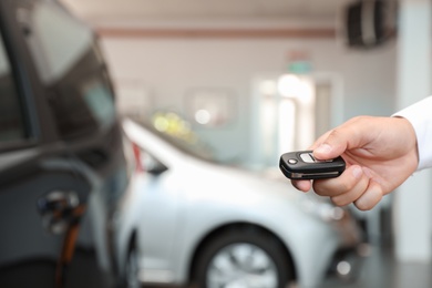 Young man turning off alarm system with car key indoors, closeup