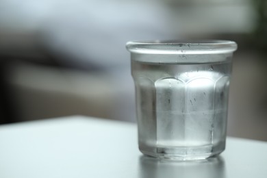 Glass of pure water on light table against blurred background, space for text
