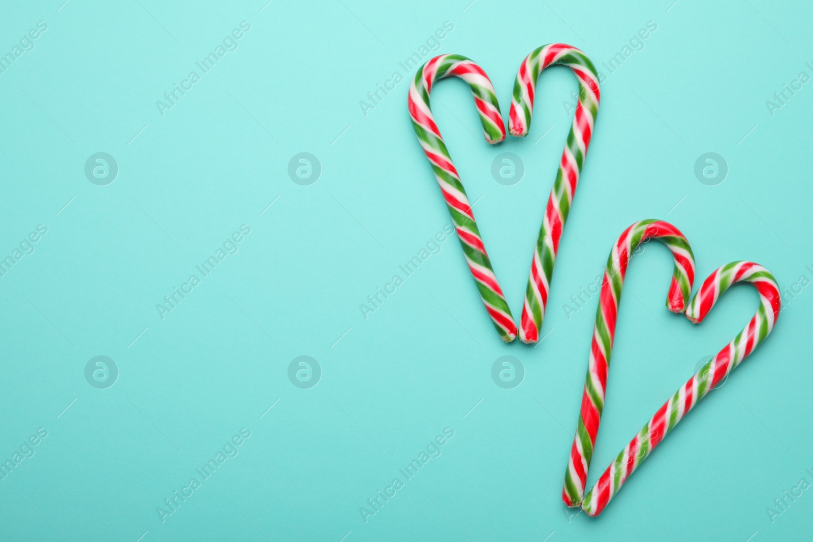 Photo of Hearts made of sweet Christmas candy canes on turquoise background, flat lay. Space for text