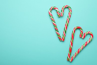 Photo of Hearts made of sweet Christmas candy canes on turquoise background, flat lay. Space for text