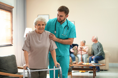 Photo of Care worker helping to elderly woman with walker in geriatric hospice