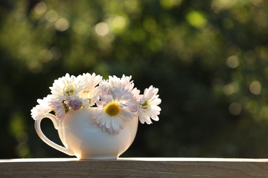Photo of Beautiful wild flowers in cup on wooden table against blurred background, space for text